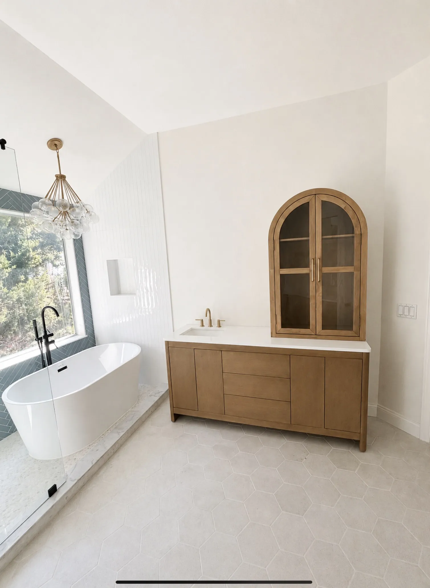 A freestanding tub beside a wood vanity and an arched wood cabinet.