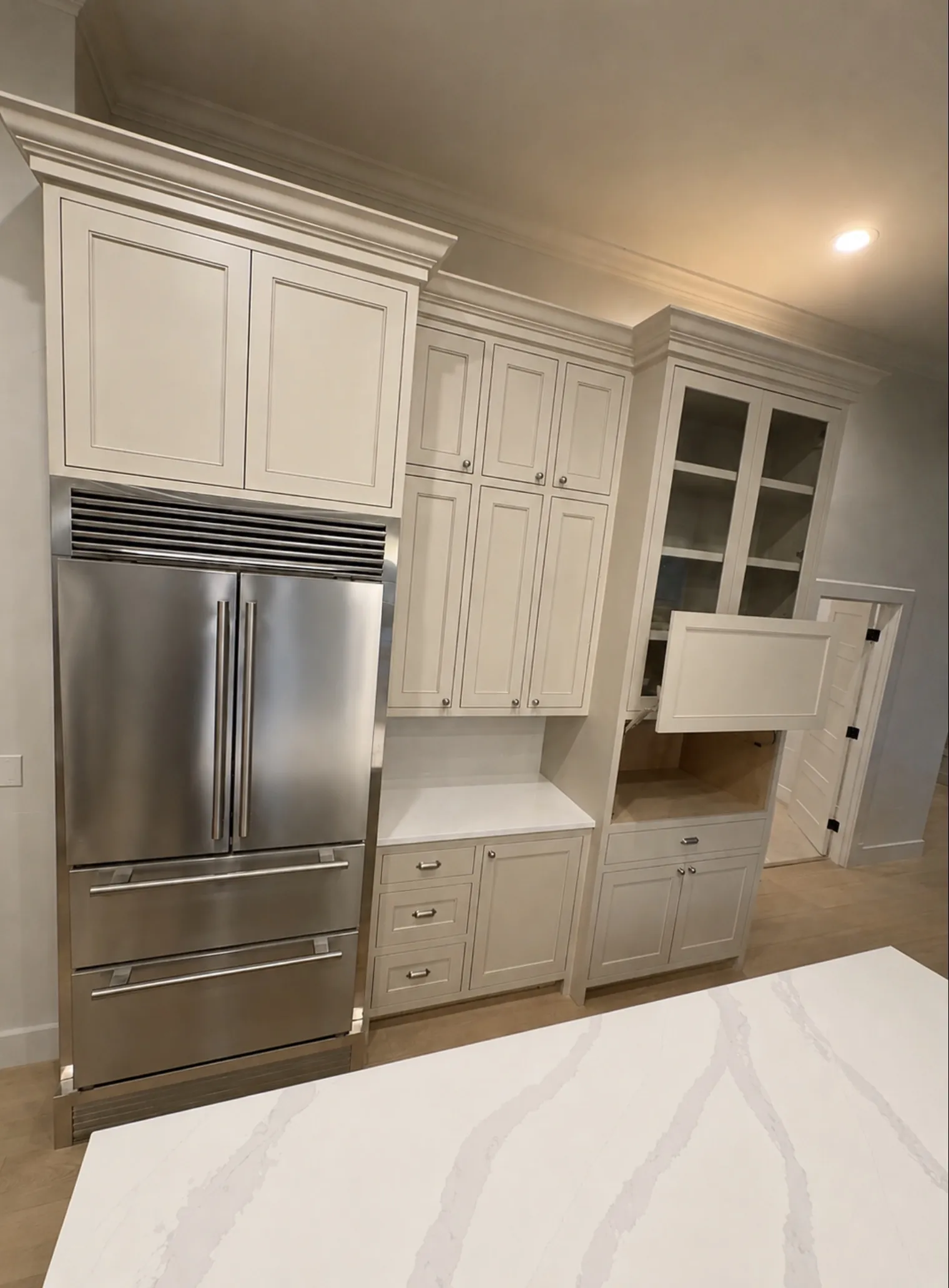 Painted cabinetry with glass uppers, a built-in pantry wall and a stainless refrigerator.