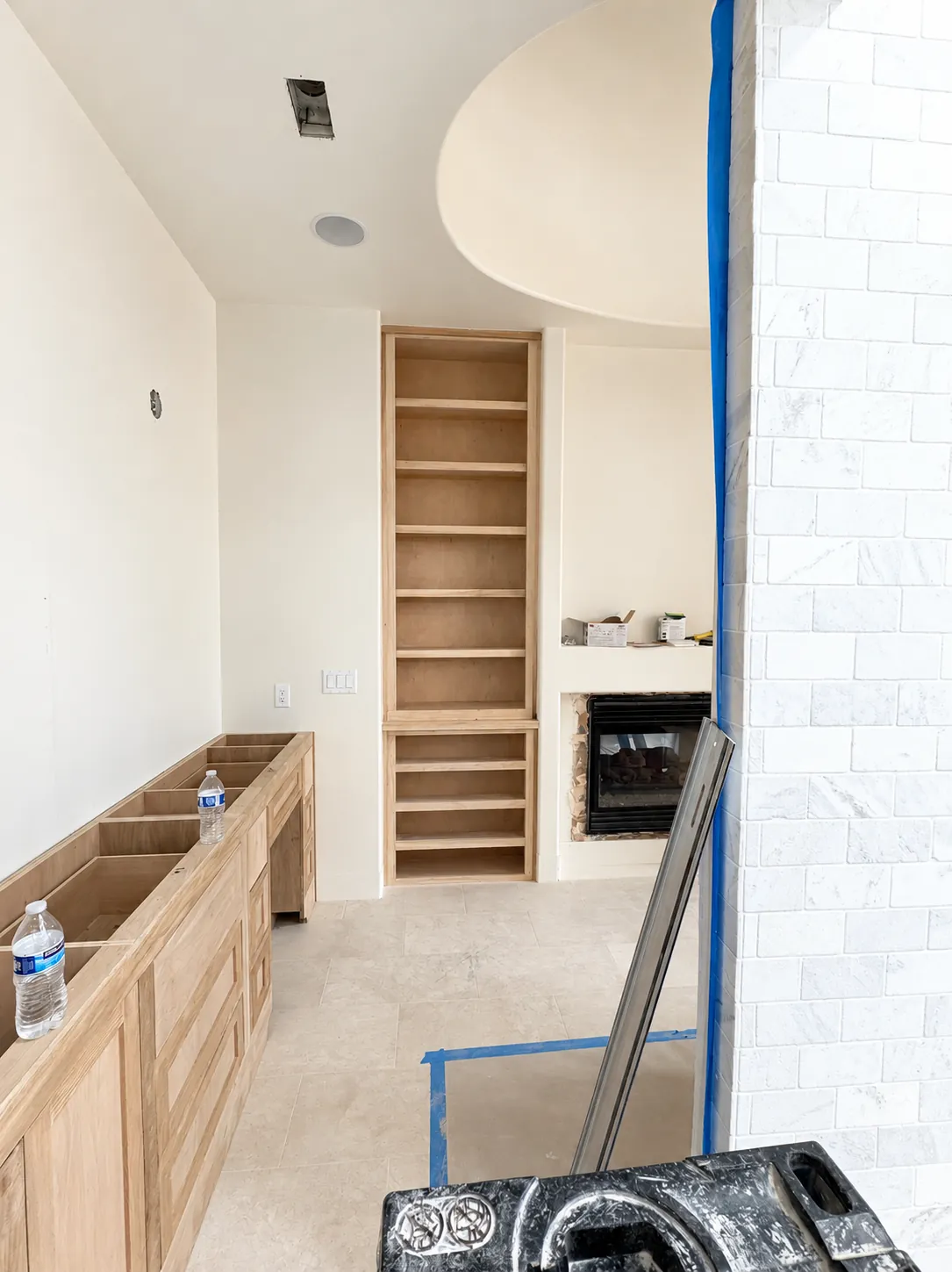 A primary bath under construction, with unfinished wood vanity cabinets, open shelves and a fireplace